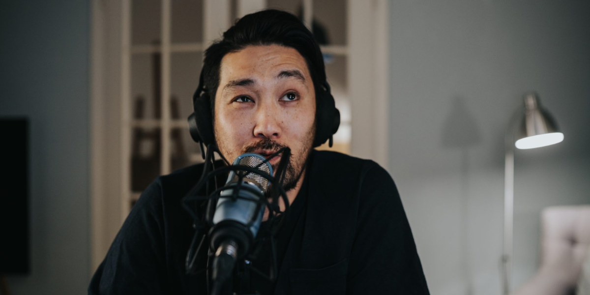 young man with goatee/mustache wearing a headset and in front of a podcast mic