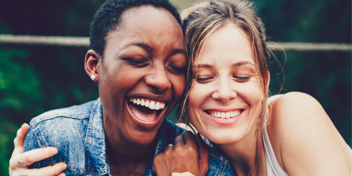 close up of two smiling laughing young women - one Black; one white