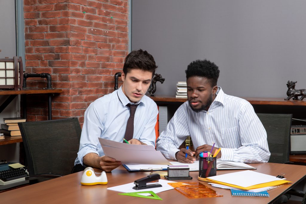 front view of two youngish businessmen looking at papers together in an office setting.